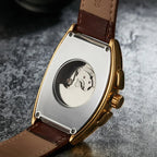 Watch with brown leather strap and visible mechanical movement on a textured gray surface
